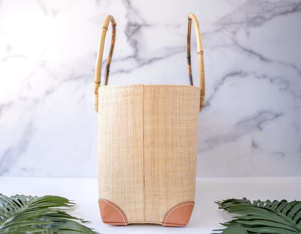 End View of the Shebobo Bebe Straw Bag with Bamboo Handles against a clean white and marble background with palm leaves