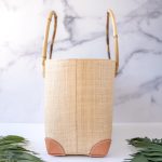 End View of the Shebobo Bebe Straw Bag with Bamboo Handles against a clean white and marble background with palm leaves