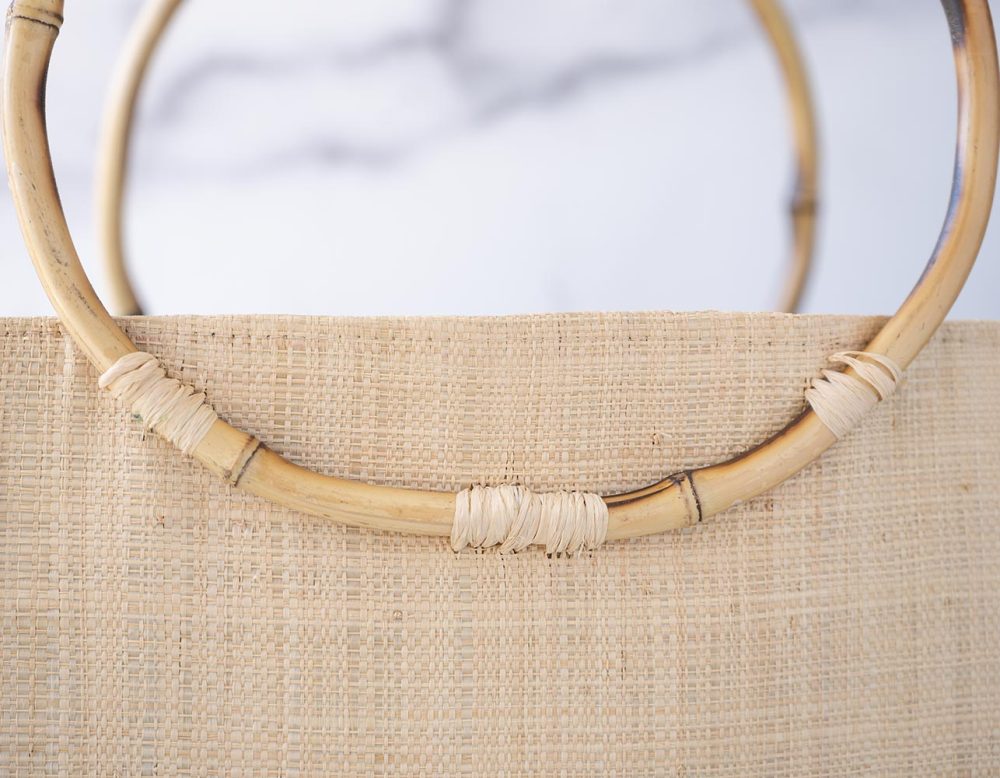 Top Closeup View of the Bamboo Handles of the Shebobo Bebe Straw Bag with Bamboo Handles against a clean white and marble background with palm leaves