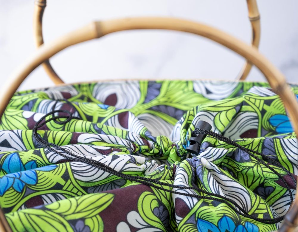 Top Closeup Open View of the of the Shebobo Bebe Straw Bag with Bamboo Handles against a clean white and marble background with palm leaves