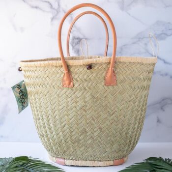 The Aravola Round Basket by Shebobo on a clean white and marble background with palm leaves