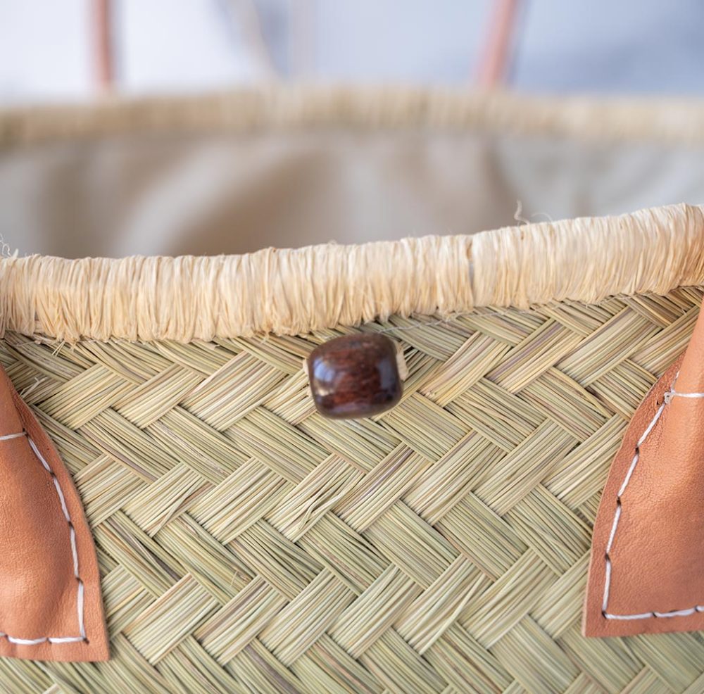 Closeup top view of the Aravola Round Basket by Shebobo on a clean white and marble background with palm leaves