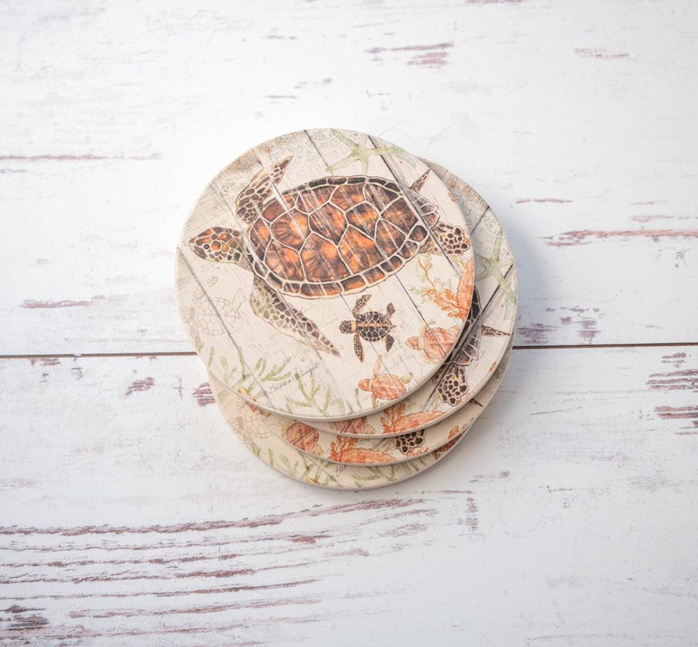 CounterArt & Highland Home Shoreline Shells coaster set of 4 stacked with colorful blue crab and sitting on top of a white rustic wood background