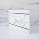 Angled View of the Life is Like a Reflection Wooden Accent Sign by Gia Roma Against a Rustic Wooden Backdrop