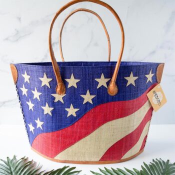 American Flag Raffia Tote Bag by Shebobo Against a Marble and Clean White Background with Palm Leaves