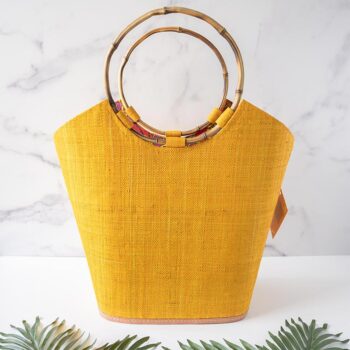 Shebobo Carmen Color Straw Bucket Basket Bag in Saffron Against a Marble and Clean White Background with Palm Leaves