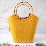 Back View of the Shebobo Carmen Color Straw Bucket Basket Bag in Saffron Against a Marble and Clean White Background with Palm Leaves