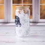 Left side view of the Mama Bear glass tumbler with a mama bear and floral pattern on a rustic background with kitchen window