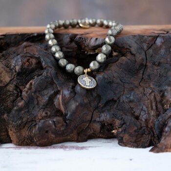 Lenny & Eva Pyrite Beaded Cross Token Stretch Bracelet back view resting on a piece of wood with a rustic background