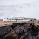 Left View of the Lotus & Luna Song of Selene Moonstone bracelet laying on a piece of wood with white rustic wood background