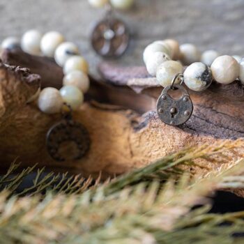 Amazonite Beaded Bracelet with Charm Collection On a Piece of Wood with Greenery Around It