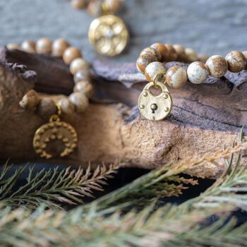 Scenic Jasper Beaded Bracelet with Charm Collection On a Piece of Wood with Greenery Around It