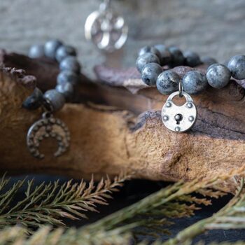 Collection of the VB&CO Designs Labradorite Beaded Bracelet with Charm Hanging Over Wood with Greenery Around It