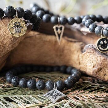 Front View of the VB&CO Designs Lava Beded Bracelet with Charm Collection Hanging Over Wood with Greenery Around