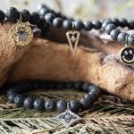 FDront View of the VB&CO Designs Lava Beded Bracelet with Charm Collection Hanging Over Wood with Greenery Around
