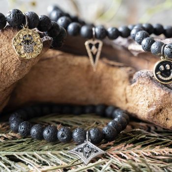 FDront View of the VB&CO Designs Lava Beded Bracelet with Charm Collection Hanging Over Wood with Greenery Around