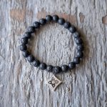 Top View of the VB&CO Designs Lava Bead Bracelet with Flower Charm on a Rustic Piece of Wood