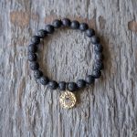 Top View of the VB&CO Designs Lava Bead Bracelet with Hamsa Charm on a Rustic Piece of Wood