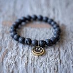 Front Closeup View of the VB&CO Designs Lava Bead Bracelet with Smiley Charm on a Rustic Piece of Wood