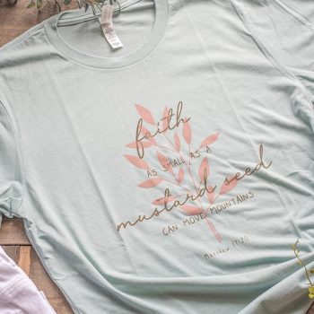 Top view of the Lemon Morraine's Faith CanMove Mountains Women's Graphic Tee on a wooden backdrop with sandals and shorts