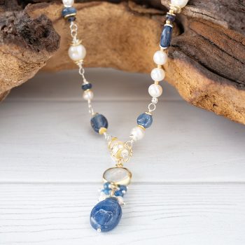 Anne Vaughn Designs Seaside Gemstone Collage Necklace Hanging on a Piece of Wood with White Rustic Wood Background