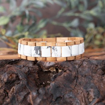 Front View of the Nordic Wood Wooden Bracelet in Maple Laying on a PIece of Wood with Greenery anda Rustic Background Behind