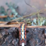 Men's two coasts wooden bracelet in liatris by Nordic Wood laying flat on a piece of wood with rustic background and greenery