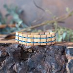 The men's two coasts wooden linen bracelet by Nordic Wood on a piece of wood with rustic background and greenery