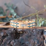 Back view of the men's two coasts wooden bracelet by Nordic Wood on a piece of wood with rustic background and greenery