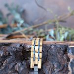 Men's two coasts wooden bracelet by Nordic Wood laying flat on a piece of wood with rustic background and greenery