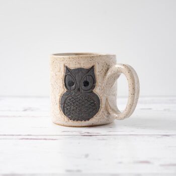 White Squirrel Clayworks stoneware ceramic owl coffee mug on white top with rustic white wood background