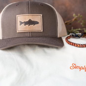 Front view of the tee of the FLats Sunational Set of the RANGE LEather Trout Hat, Surf Rider Dawn Patrol Beaded Bracelet and SImply Florida; Hook, Line & Sinker Tee Against a Rustic Background with Greenery