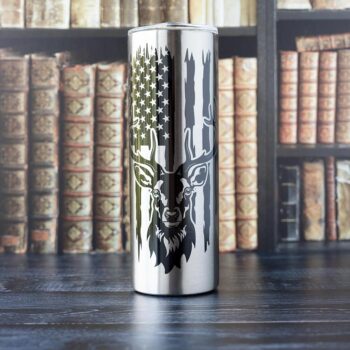Front view of the Buck & American Flag stainless skinny tumbler by Emma K designs on a office type background with books