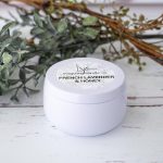 Closed French Lavender & Honey flower tin can candle on a rustic table with greenery in th ebackground