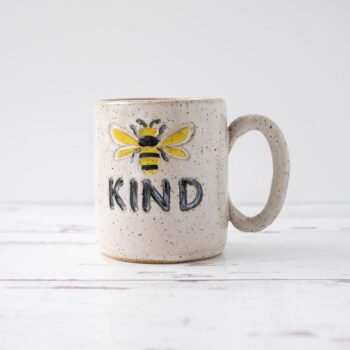 White Squirrel Clayworks stoneware ceramic bee kind coffee mug on white top with rustic white wood background