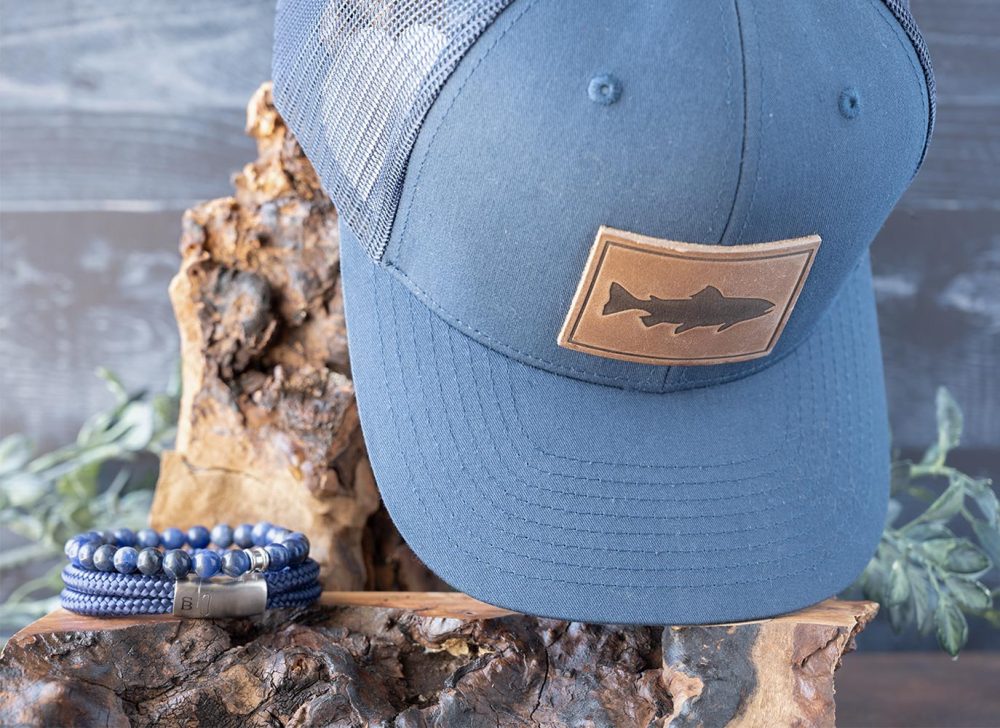 Two Shore Sunsational Set Collection of the Trout Hat in Navy and the Rope Lake Bracelet and Beaded bracelet in Navy on Wood and Against Rustic Background