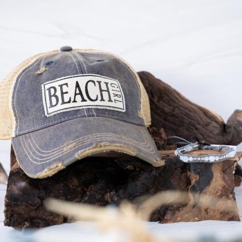 Perfect Pairing of the Beach Girl Distressed Trucker Hat and the Moonstone Mermaid Blessings Coconut Clasp Bracelet on Rustic Wood and White Background