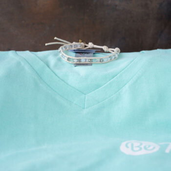 The Shine Bright Perfect Pairing Collection of the Twinkling Sky Moonstone Bracelet andthe Be Kind V-Neck Women's Tee Against a Rustic Backdrop