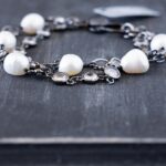 Side closeup view of the Sandy Shores womens' peacock pearl bracelet clasp on a dark piece of rustic wood
