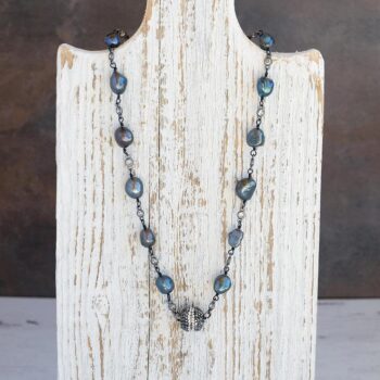 View of the Coastal Beach Pearl Necklace hanging on a rustic white piece of wood with dark rustic background