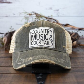 Country Music & Cocktails distressed trucker cap perfect for the southern lifestyle against a rustic background