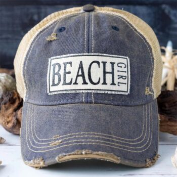 Women's Beach Girl distressed trucker hat against a rustic background and greenery