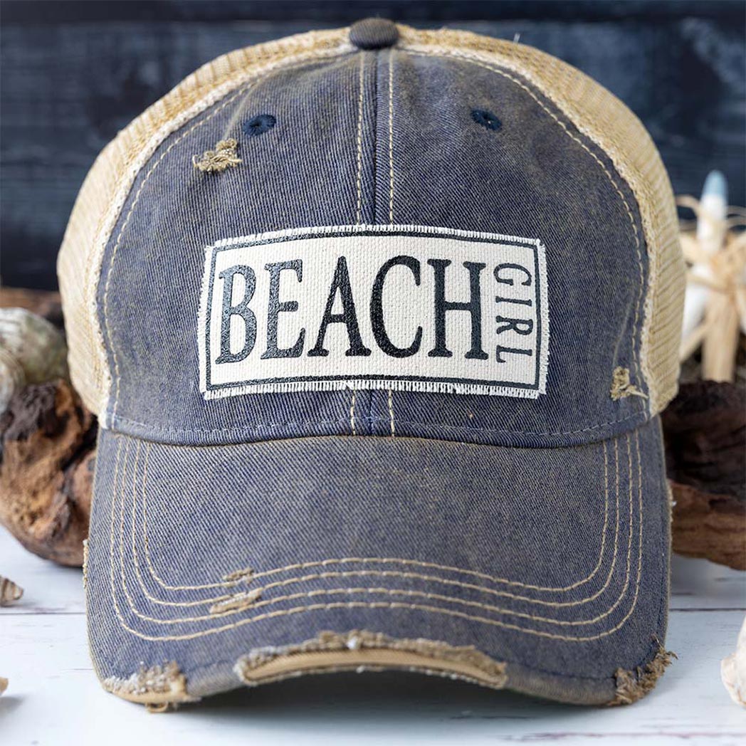 Women's Beach Girl distressed trucker hat against a rustic background and greenery