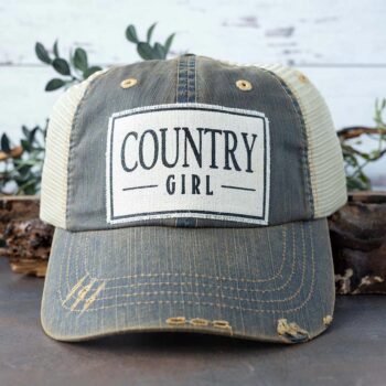 Women's Country Girl distressed trucker hat against a rustic background and greenery