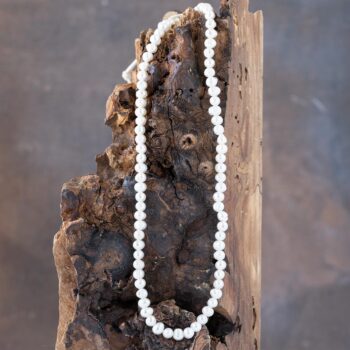 Danlge view of the Sugary Sands Self Love Pearl Necklace Laying on a Rustic Piece of Wood