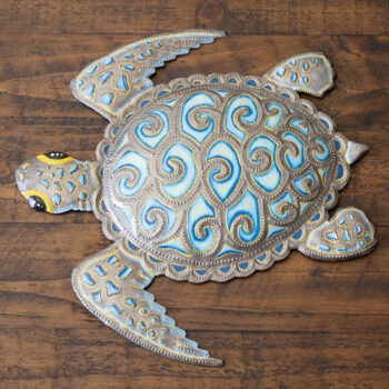 Top view of the Bright Eyed Turtle Haitian steel drum wall art in turquoise & gold on a dark rustic wood background