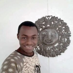Haitian artist Jonas Soulouque against a white wall hanging a sun wall art piece he created