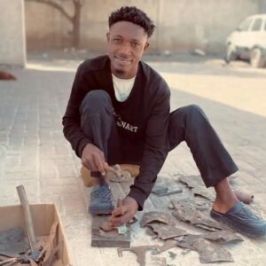 Haitian artist Orilien smiling as he works on a Haitian Wall Art piece outside