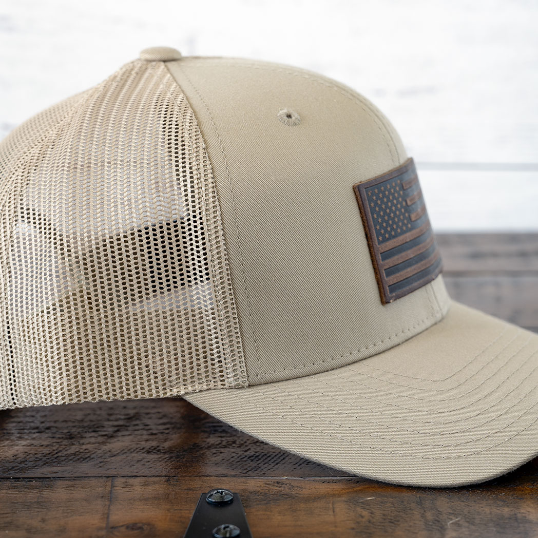 Right angle of the RANGE Leather American flag leather patch hat in tan against a rustic wood background