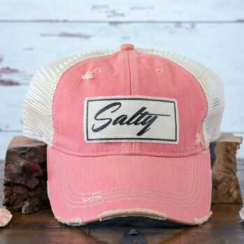 Vintage Life Salty women's distressed trucker cap in sunsetpink leaning on a piece of wood against a rustic background
